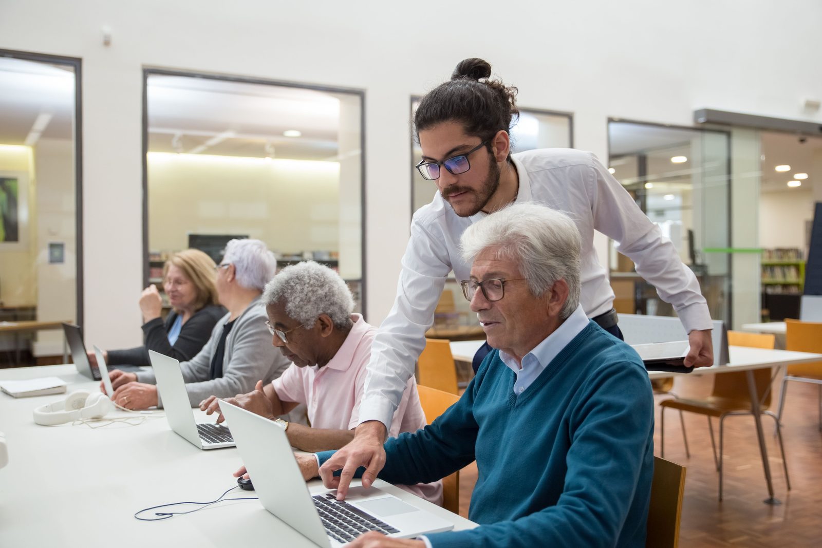 Ein Trainer hilft zwei älteren Teilnehmenden geduldig am Laptop